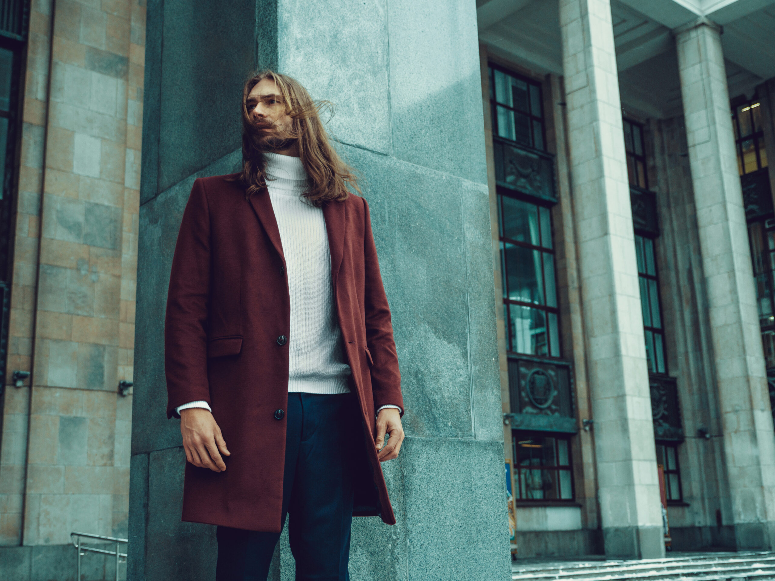 Handsome confident well dressed man with beard posing outdoors looking away. Fashionable rich male model in red winter coat and white sweater